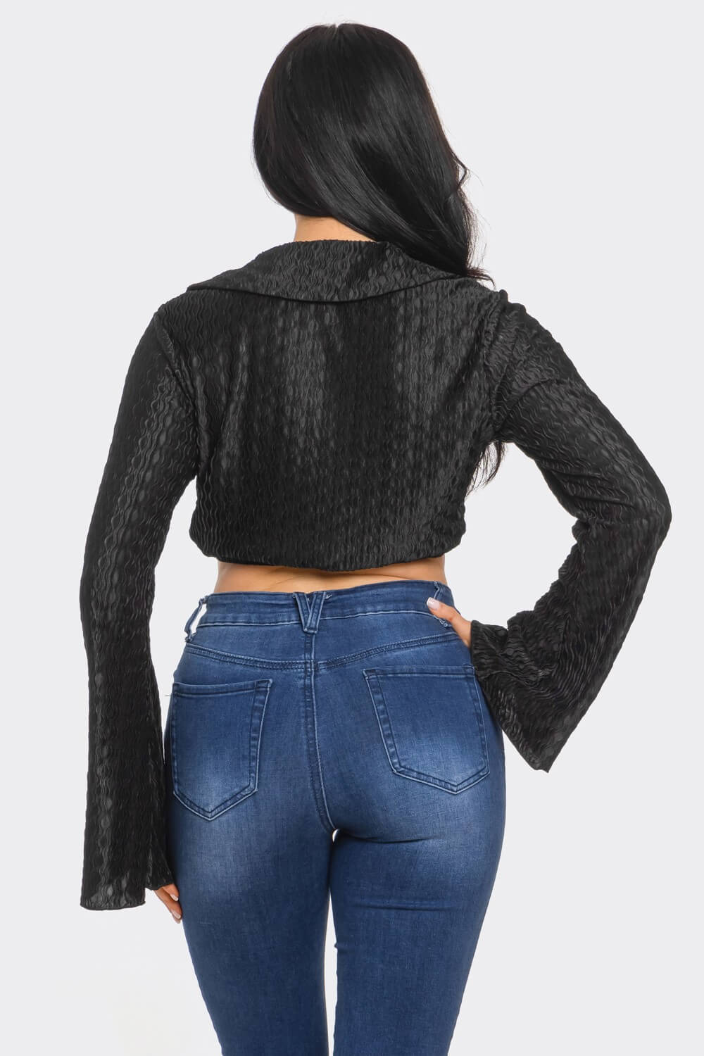 Person wearing a black textured jacket and blue jeans on a white background