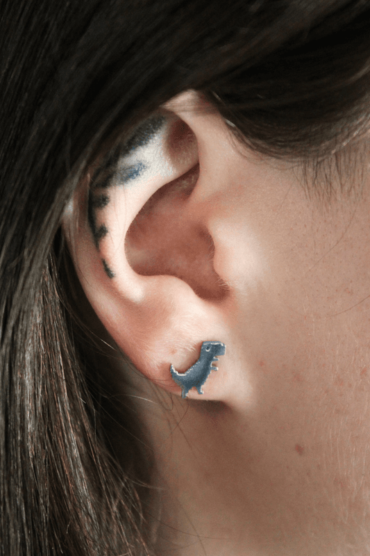Close-up of an ear with a dinosaur-shaped earring and tattoos on the earlobe.